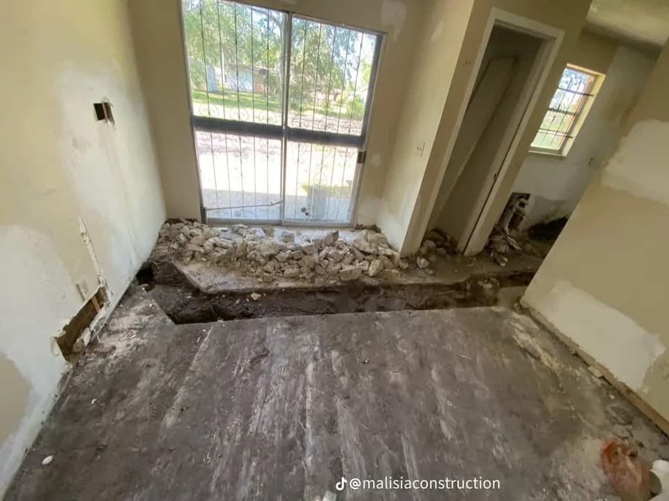 Empty room interior under construction with concrete floor, debris piled against windows, and white walls