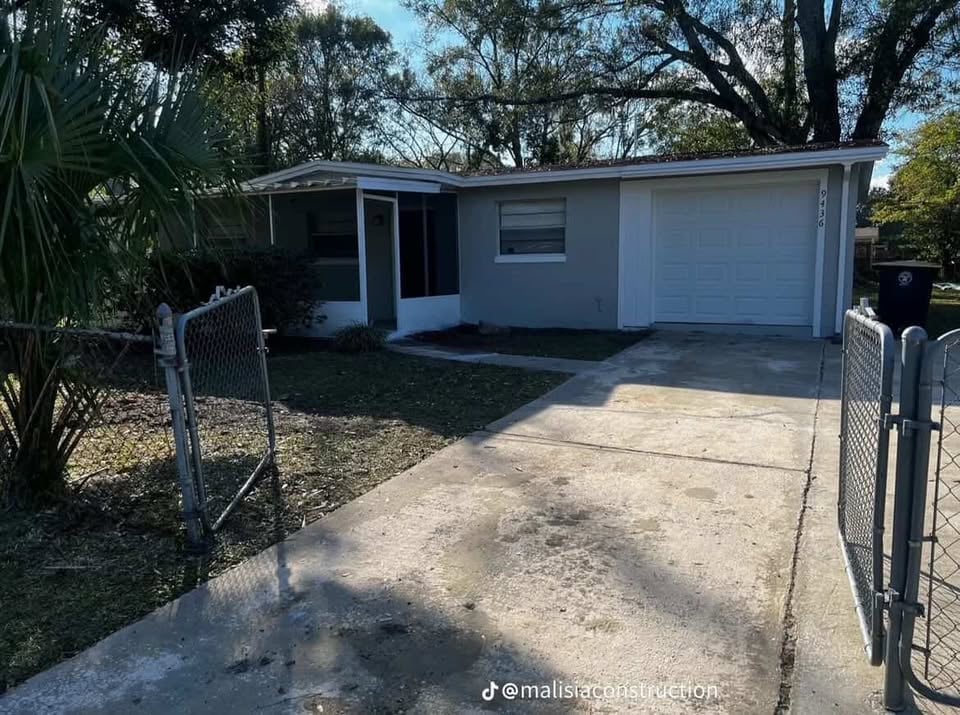 Single-story white house with attached garage, concrete driveway, metal gate, and mature trees on sunny day