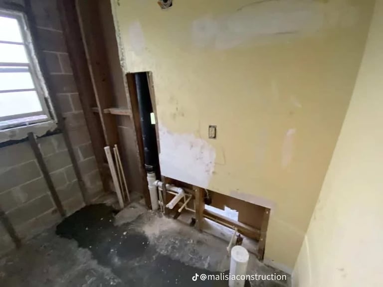Unfinished interior room with yellow walls, construction materials, wooden headboard, window on left, and debris on floor