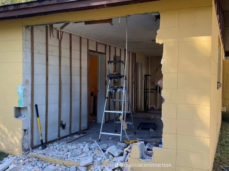 Construction site showing interior renovations with drywall removal, metal studs, ladder, and debris on floor