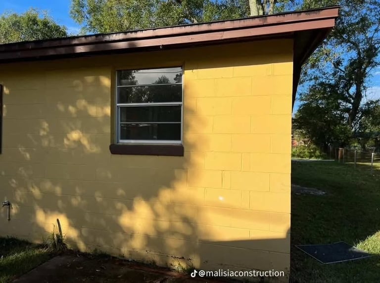 Bright yellow modern shed with dark trim roof, rectangular window, and yellow garage door in sunny outdoor setting with trees